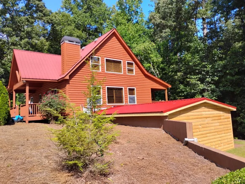 Finished attached storage addition with D-log siding and a red metal roof beside the matching North Georgia home
